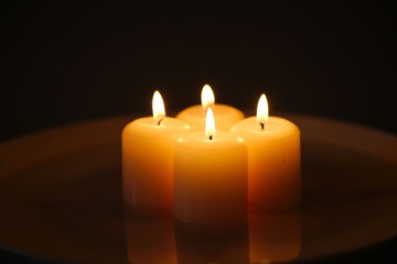 Four burning candles with reflection on a white plate with water against dark background
