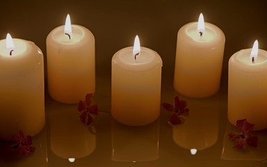 Group of burning candles with water reflection and purple flowers