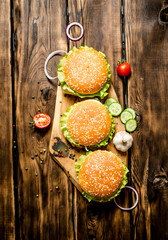 Three finished Burger with meat and vegetables on wooden stand.