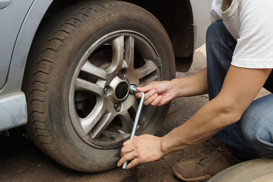 The man changes the punctured wheel of the car.