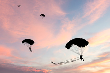 Silhouet van parachute en vliegtuig op zonsondergangachtergrond