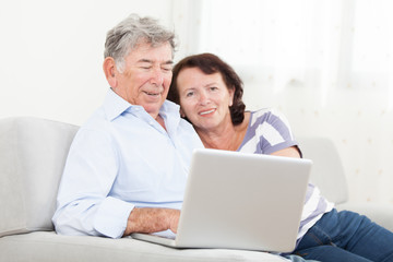 Fototapeta na wymiar Senior couple laughing while using laptop