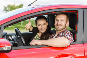 Two young smiling people in a red car