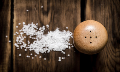 Salt with coarse salt. On wooden background.