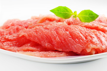 Fresh pork meat on a white plate. Sprig of basil on top of the meat.