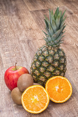 Orange oranges, pineapple, kiwi and apple on a wooden background