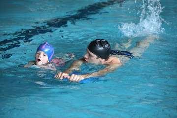 swimming lesson - child practicing flutter kick with kick board with instructor in swimming pool