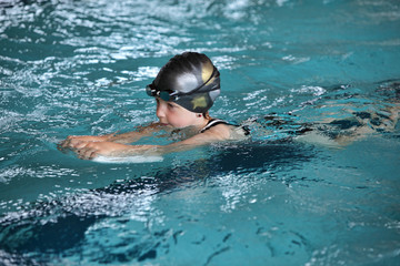 Close up of child practicing flutter kick with kick board in indoor swimming pool