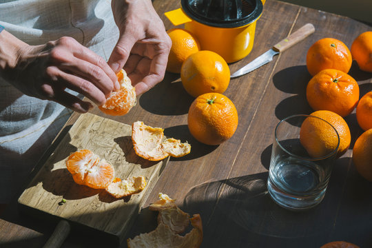 Close up of woman's hand peeling ripe tangerines on wooden table