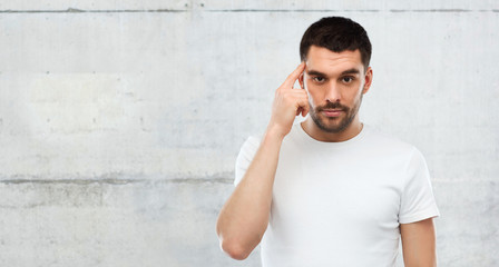 man with finger at temple over gray wall
