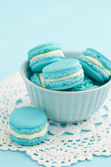 Three turquoise macarons with buttercream filling in little blue bowl