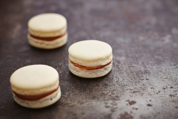 Three white macarons with caramel filling on dark background