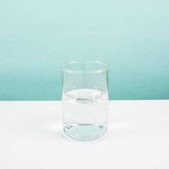 Half empty or half full glass of water on white table. (For positive thinking when see the glass is half full.)