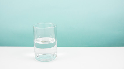 Half empty or half full glass of water on white table. (For positive thinking when see the glass is...