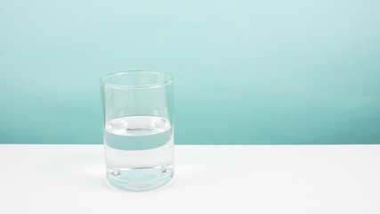 Half empty or half full glass of water on white table. (For positive thinking when see the glass is half full.)