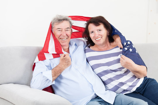 Happy senior couple seating wrapped in American flag