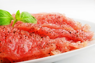 Fresh pork meat on a white plate. Sprig of basil on top of the meat.