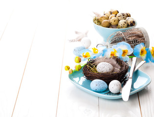 table decoration with easter eggs nest on plate, on white wooden