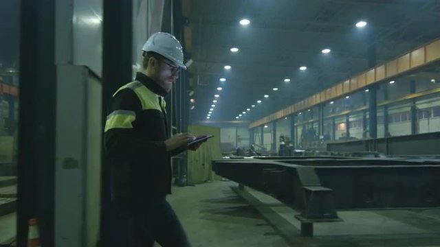 Engineer in hardhat is moving through a heavy industry factory with a tablet computer. Shot on RED Cinema Camera.