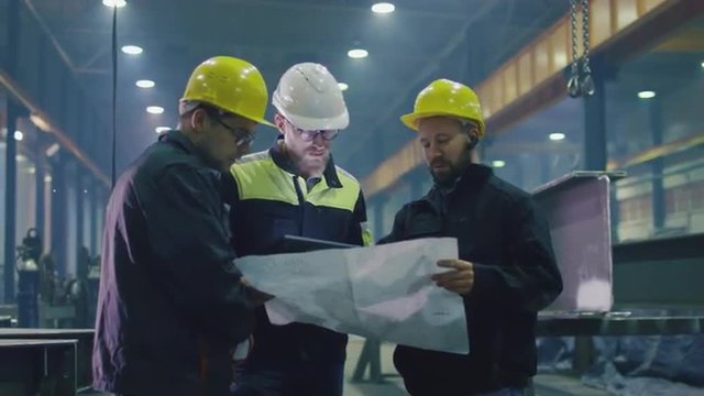 Team of workers at a heavy industry factory have a conversation while looking at a blueprint. Shot on RED Cinema Camera.