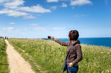 Woman taking Photos with her Mobile Phone on a Coast Path in Cornwall