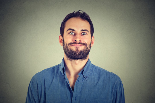 Crazy looking man making funny faces isolated on gray wall background .