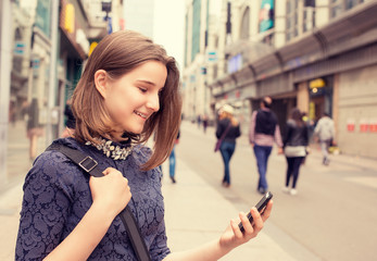 happy girl walking and texting on the smart phone in the street