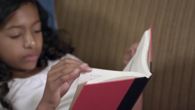 Panning shot fo a young girl with bandaged knee reading.