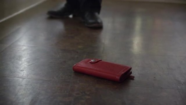 Tight shot of wallet, on the ground in a grocery store, is picked up by man.