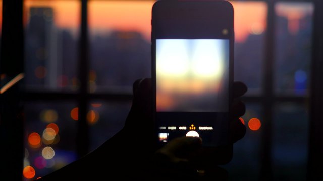 Woman makes a picture from the window with his mobile phone. Night light bokeh blurred city background. 4k