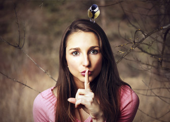Young woman with a bird on his head making the gesture of silence.
