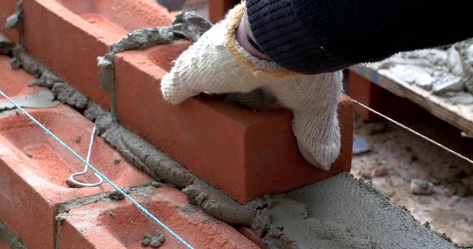 Handheld footage of a bricklayer laying bricks and building an exterior wall. No face visible or other identifiable features