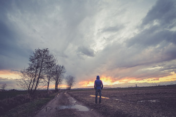 Man under a cloudy sky in the country watching the sunset