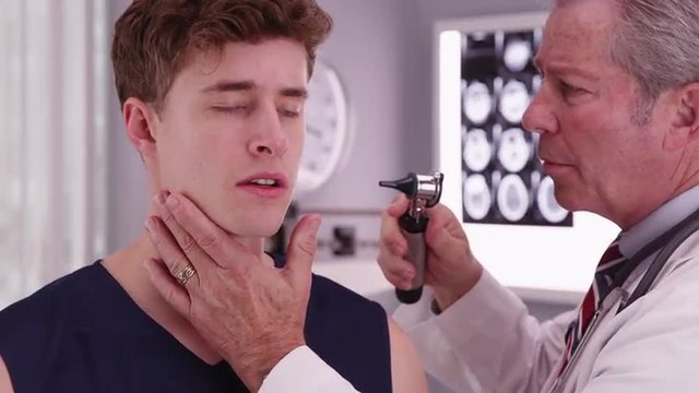 Senior doctor checking sports athlete's ear with an otoscope