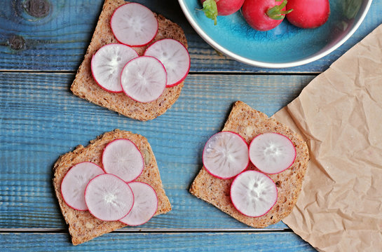 Radishes and whole grain bread on blue table. Vegetarian food concept, healthy life style