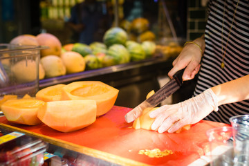 market stand with fresh fruits, woman's hands cutting fresh melon, selective focus