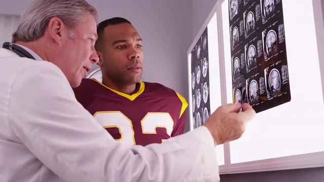 African sports athlete looking at x-rays with Caucasian doctor