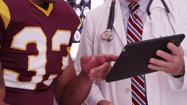 Close-up of medical doctor looking at tablet computer with sports athlete