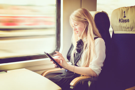 Blond girl on a train with a tablet traveling first class.