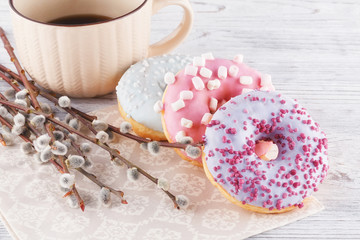 Three donut, a cup of coffee and willow on a white table