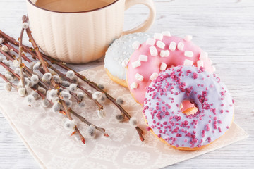 Three donut, a cup of coffee and willow on a white table