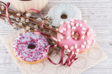 Three donut, a cup of coffee and willow on a white table