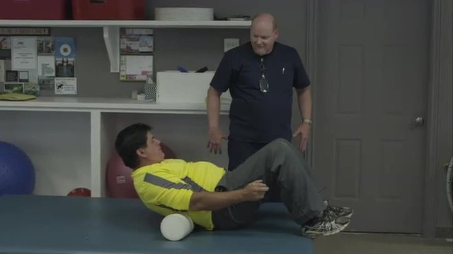Man working with physical therapist on back roller.