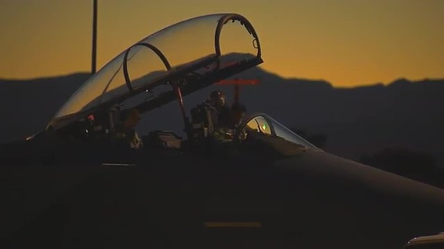 Fighter pilots prepare their jets on a runway at dusk.