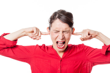 noise and hearing concept - enraged young woman screaming, plugging her ears to refuse listening to...