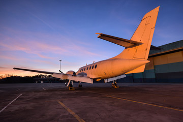 Naklejka na ściany i meble Small aeroplane infront of aircraft hangar during sunrise