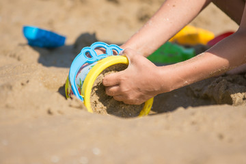 The baby is gaining a bucket in the wet sand, close-up