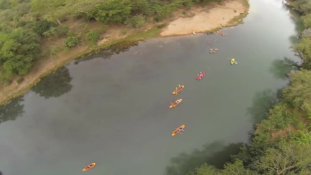 Aerial of 10 canoes being paddled down a river between banks of bush-veld in Africa.