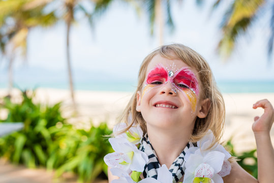 Smiling little girl with vivid face painting. Fancy dress party on the beach.