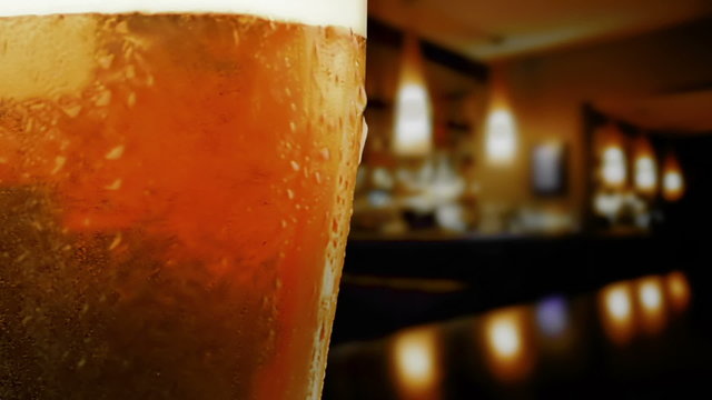 pouring fresh beer with foam into glass on table into pub background, zoom in movement camera